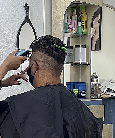 Corte desvanecido a máquina en la nuca de un cliente, con repisa de productos al fondo.