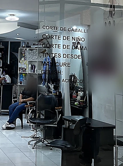 La vitrina del salón con la lista de servicios en vinil blanco y un sillón negro de corte adentro.